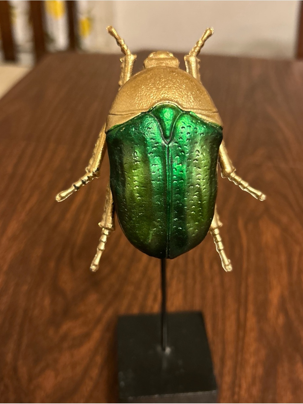 Green and gold beetle on wood base